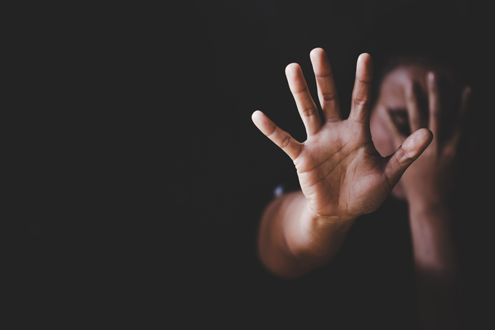 A woman covering her face and holding her hand up to the camera.