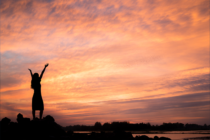 The silhouette of a person raising their arms outside.