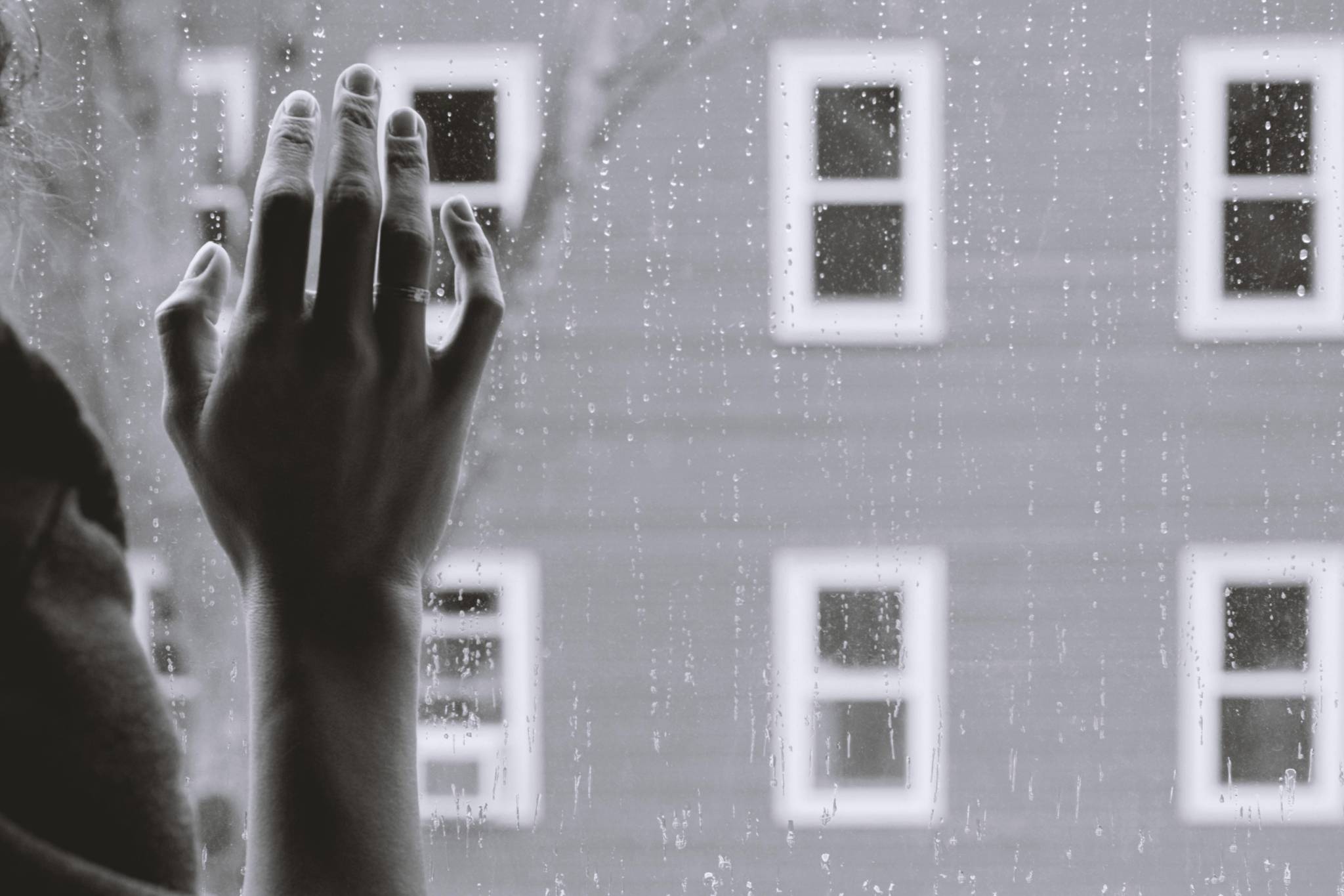 A hand on a rainy window looking outdoors.