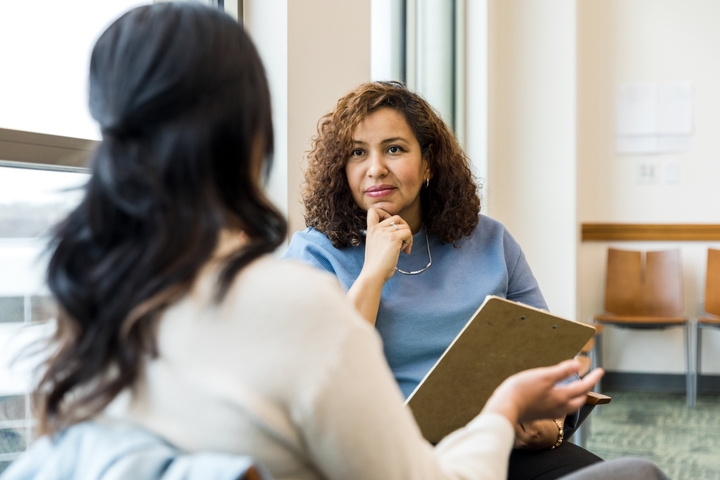 A woman holding a clipboard looking at a woman sitting on a couch.