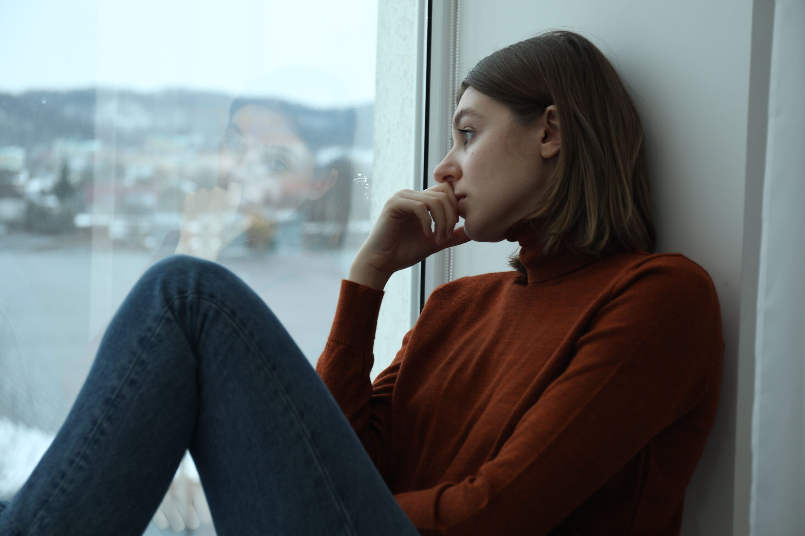 Leaving an Abusive Relationship: 5 Steps to Safety Woman sitting thoughtfully near a window while considering leaving an abusive relationship
